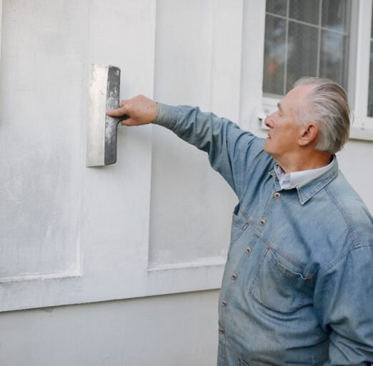 Old man near building. Senior in a blue shirt. Grandfather with repair tools.