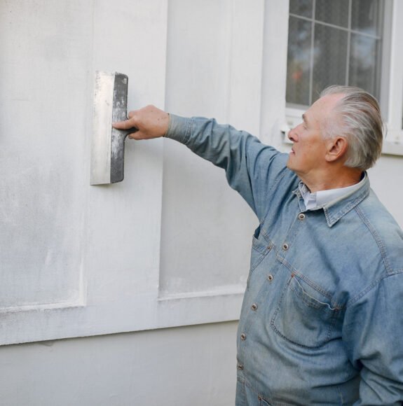 Old man near building. Senior in a blue shirt. Grandfather with repair tools.