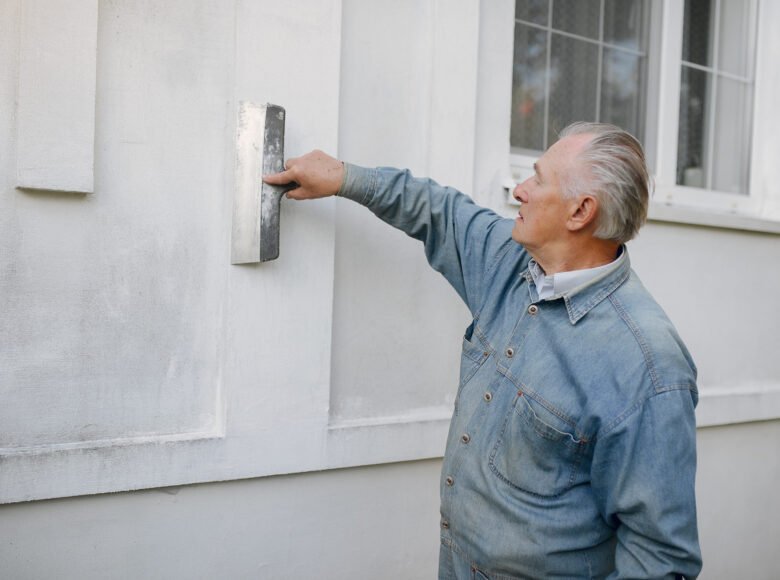 Old man near building. Senior in a blue shirt. Grandfather with repair tools.